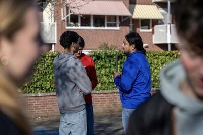 Groep jonge mensen in gesprek op straat, met appartementen op de achtergrond.