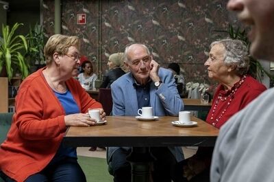 Drie mensen in een café genieten van een gesprek met koffie op tafel. Een man en twee vrouwen, lachend en ontspannen.